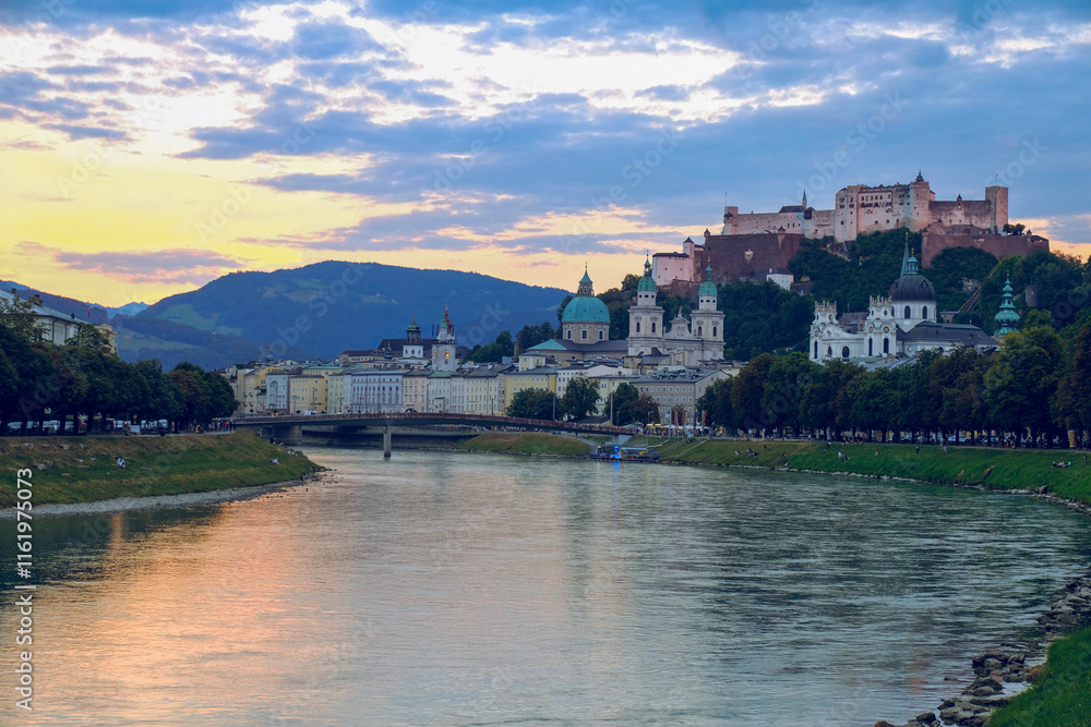 The city of Salzburg with historical buildings bisected by a winding Salzach River and mountain ranges in the background