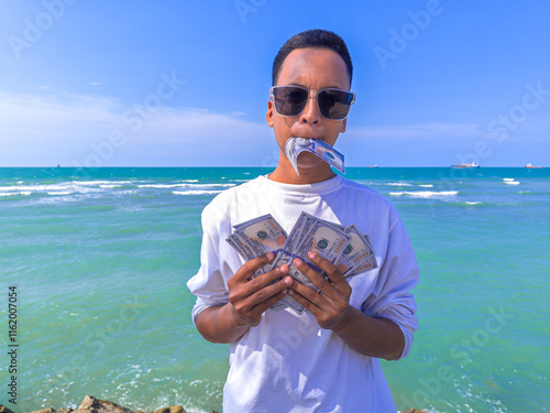 Asian guy with white shirt and wear glasses. Concept Confident man holding a 100 dollar bill in his hand, man hold 100 USD. Summer sea water background. focus on man. noisy, exposure, similar others