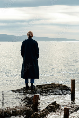 Lone woman on rrocky shore with scenic sea bay view photo