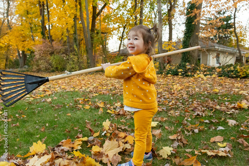 Adorable Little Preschool Girl Holding Rake in Backyard During Autumn photo