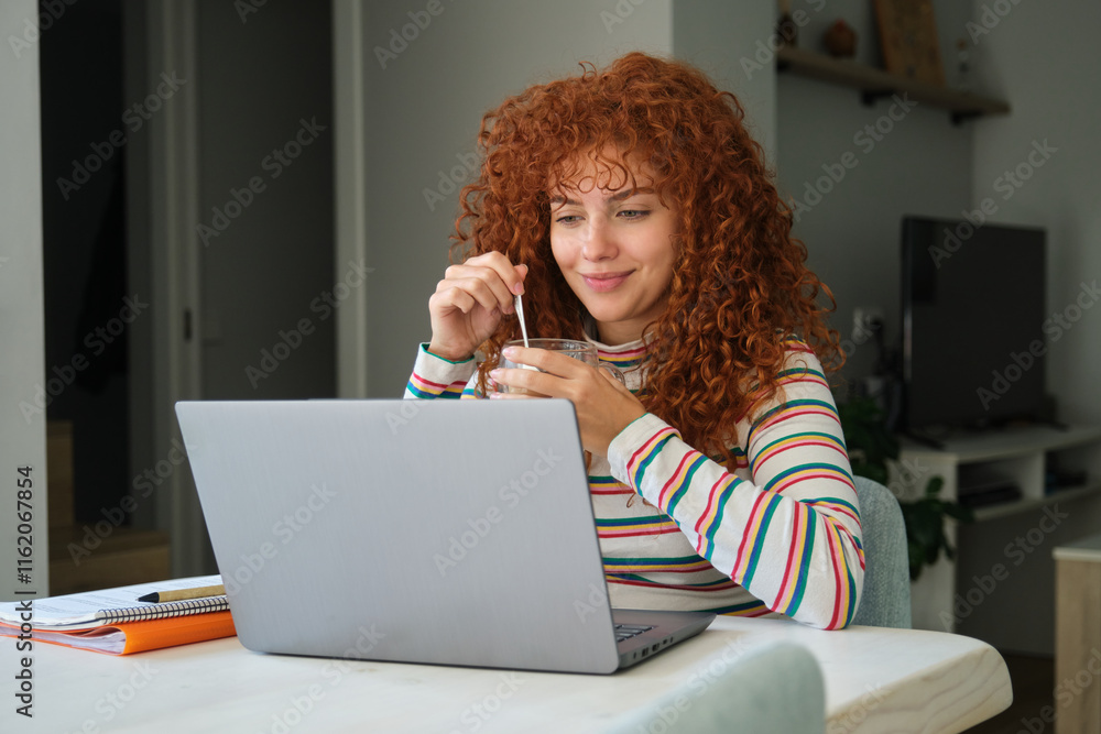 Young woman working from home drinking and looking at laptop Young woman working from home drinking and looking at laptop