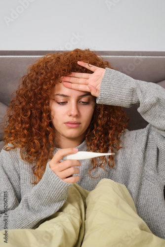 Sick woman is lying in bed and checking her body temperature photo