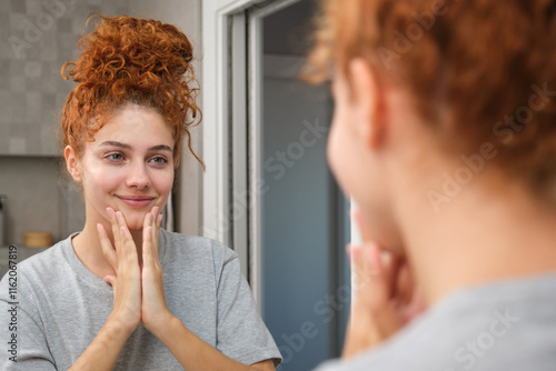 Woman admiring her face after applying skincare products in a mirror photo