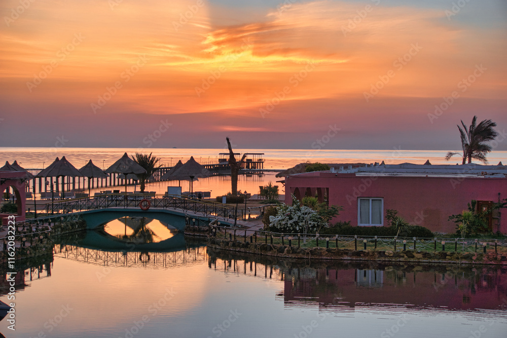 Obraz premium Fantastic sunrise in Marsa Alam over the Red Sea. visible palm trees, beach umbrellas, typical hotel buildings. Egypt, Marsa Alam 2024