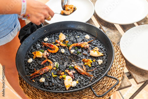 Fototapeta Naklejka Na Ścianę i Meble -  Chef serving fresh black rice paella with seafood in mallorca