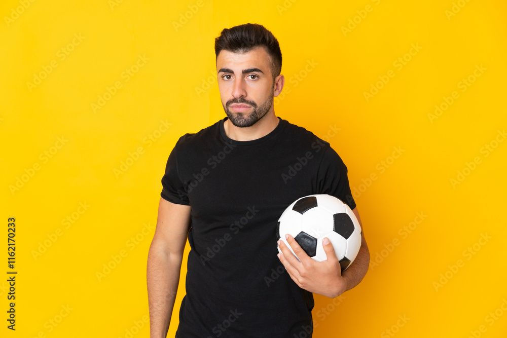 Caucasian man over isolated yellow background with soccer ball Caucasian man over isolated yellow background with soccer ball