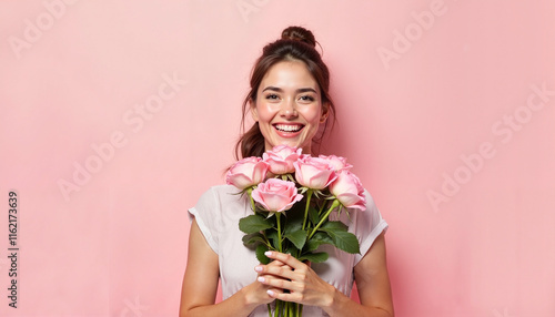 Cheerful young woman holding pink roses in front of a pastel pink background