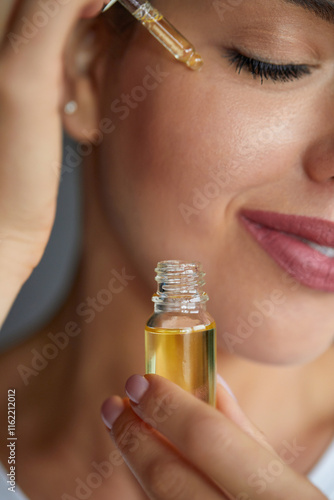 Woman Dropping Serum on Face. Model Girl Applying Serum Collagen Moisturizer from Pipette on Face close up. Positive Laughing Beautiful Woman. Concept of Face Skin Care