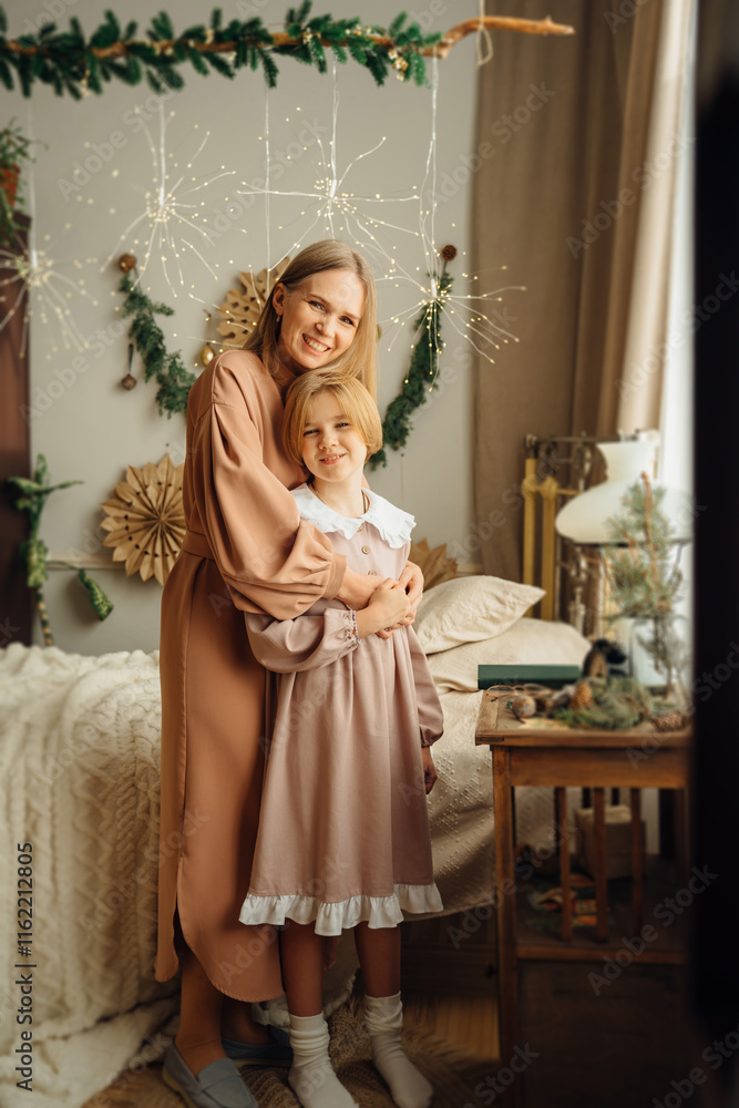 Mom and daughter in pink retro dresses hugging in a room with vintage furniture and New Year decor. The tradition of celebrating Christmas and decorating the house. Mom and daughter in pink retro dresses hugging in a room with vintage furniture and New Year decor. The tradition of celebrating Christmas and decorating the house.