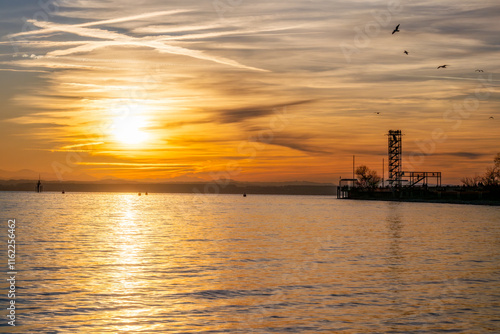 Sonnenuntergang am See mit Silhouette eines Aussichtsturms und fliegenden Vögeln photo