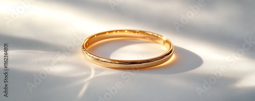 A simple gold bracelet placed on a smooth white background, reflecting bright light and showcasing crisp details. contrast, white background