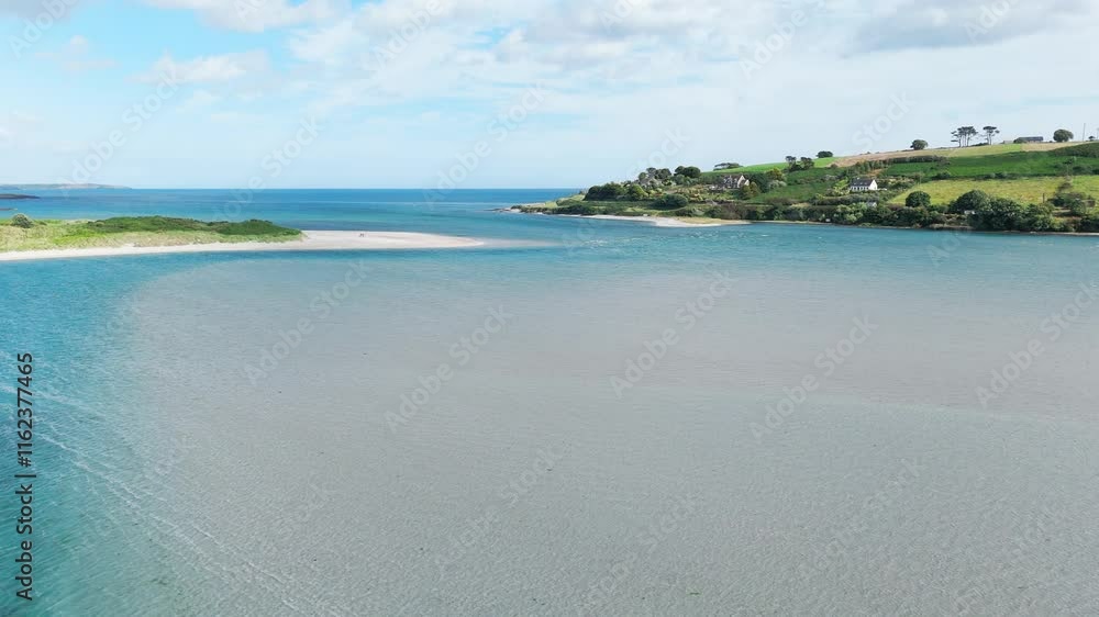 A tranquil coastal scene. A small, sandy beach is visible. The water is calm and light blue-grey. Green vegetation lines the shoreline. A tranquil coastal scene. A small, sandy beach is visible. The water is calm and light blue-grey. Green vegetation lines the shoreline.