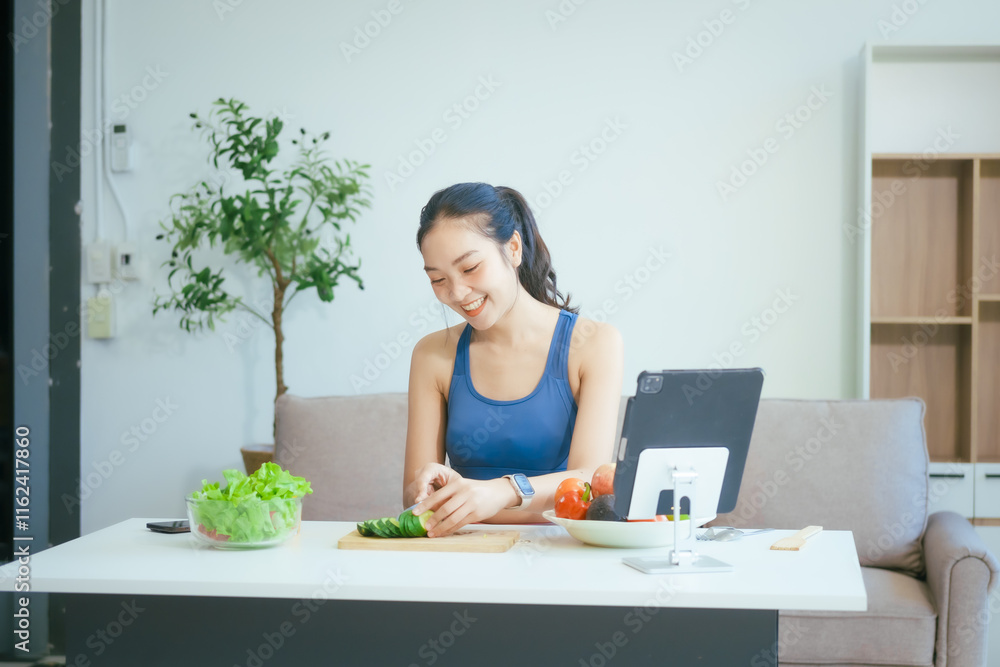A happy Asian woman in sportswear sits on a sofa at a table, enjoying a salad bowl, fruits, fresh vegetables, orange juice, and energy supplements after a home fitness workout A happy Asian woman in sportswear sits on a sofa at a table, enjoying a salad bowl, fruits, fresh vegetables, orange juice, and energy supplements after a home fitness workout