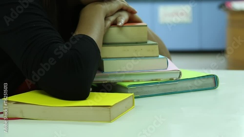 One woman take a rest and leaning on stack of books with additional colorful books spread on a white desk in a study environment photo