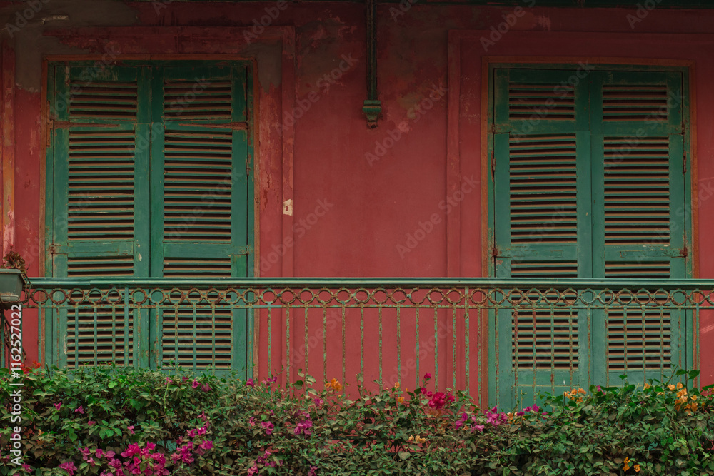 Typical house in sant Louis, Senegal. View of facade front with green blinds and colorful balcony with flowers. Red facade...