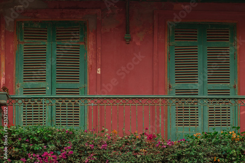Typical house in sant Louis, Senegal. View of facade front with green blinds and colorful balcony with flowers. Red facade...