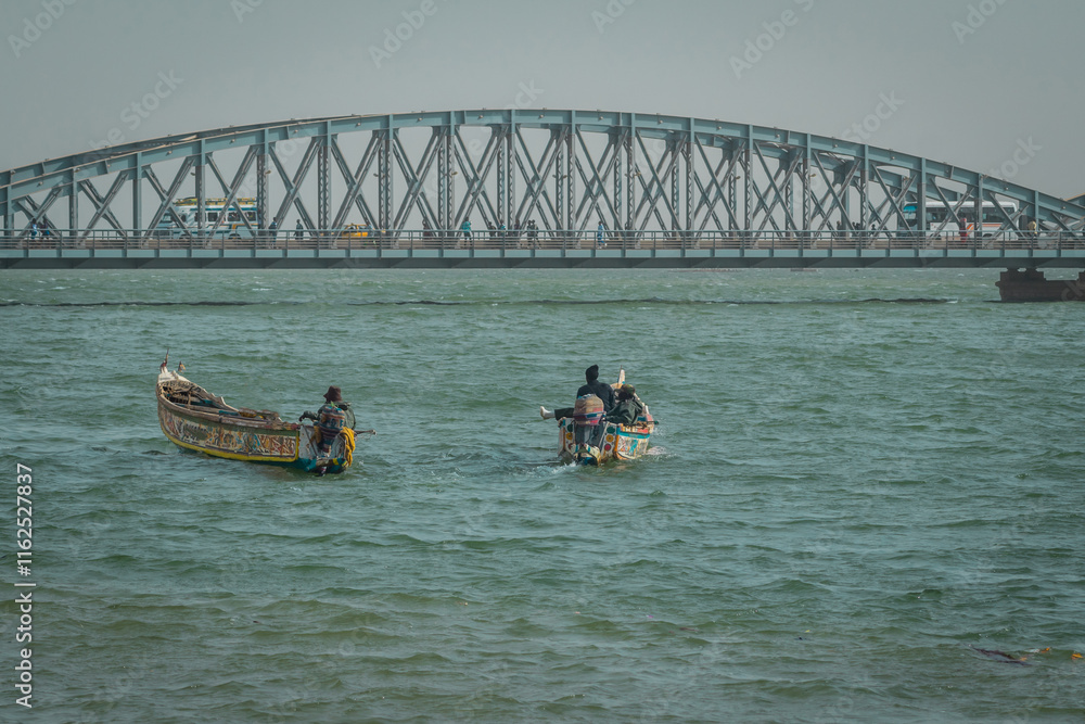 Typical senegalese fishermen with boats called pirogue floating towards famous faidherbe metal bridge over senegal river. Beautiful african postcard..