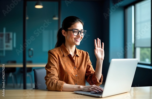 Happy Hispanic woman works in modern office. Businesswoman uses laptop for video call. Smiles, greets colleagues online. Modern office setting. Woman, laptop, video call, business, greeting, online,