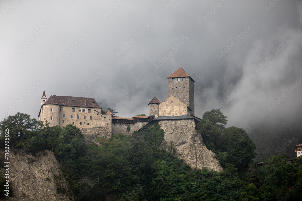 Schloss Tirol in Dorf Tirol near Meran, surrounded by a misty alpine landscape in summer. The historic castle emerges through the fog, creating a mystical and atmospheric scene. Schloss Tirol in Dorf Tirol near Meran, surrounded by a misty alpine landscape in summer. The historic castle emerges through the fog, creating a mystical and atmospheric scene.