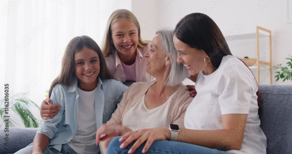 Portrait of a happy Caucasian grandmother, mother, and daughters embracing together, sitting on the sofa at home. Family love, bonding, and affection, showing strong relationships. Portrait of a happy Caucasian grandmother, mother, and daughters embracing together, sitting on the sofa at home. Family love, bonding, and affection, showing strong relationships.