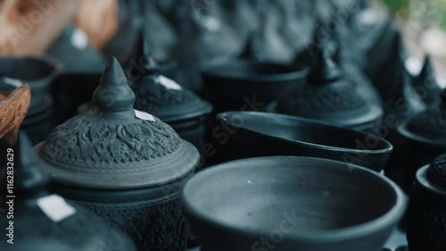 Selective focus on thai clay pots with lids standing on market shelf with with stickers with price on top. Traditional asian crafts painted in black colour representing folk art and culture.