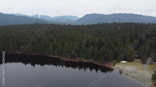 Floating above a peaceful lake surrounded by green mountains under cloudy skies