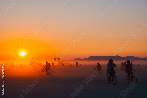Obraz na płótnie A warm orange sunset illuminates a desert festival scene with cyclists, art installations, and distant mountains in Black Rock Desert, Nevada. w salonie