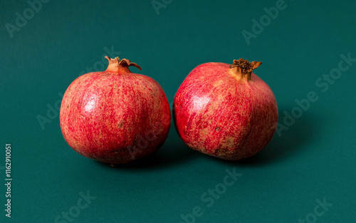 Two ripe and vibrant red pomegranates placed on a green surface. A simple and elegant composition highlighting fresh produce and natural textures.