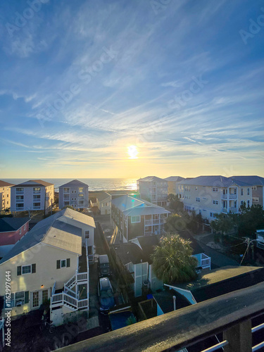 A beautiful sunrise over the Atlantic ocean with homes and condos, lush green trees, a sandy beach and ocean waves in Carolina Beach North Carolina USA