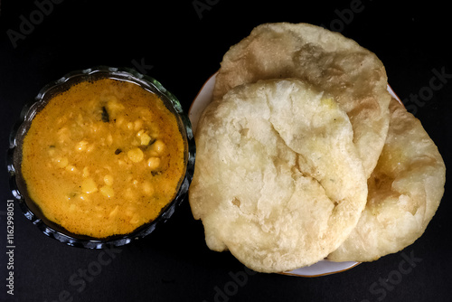 Homemade Daalpuri with Sweet Chana Daal. Oil fried puffed flat bread made with healthy wheat flour and chana masala served in a steel plate and glass bowl. Indian cuisine.