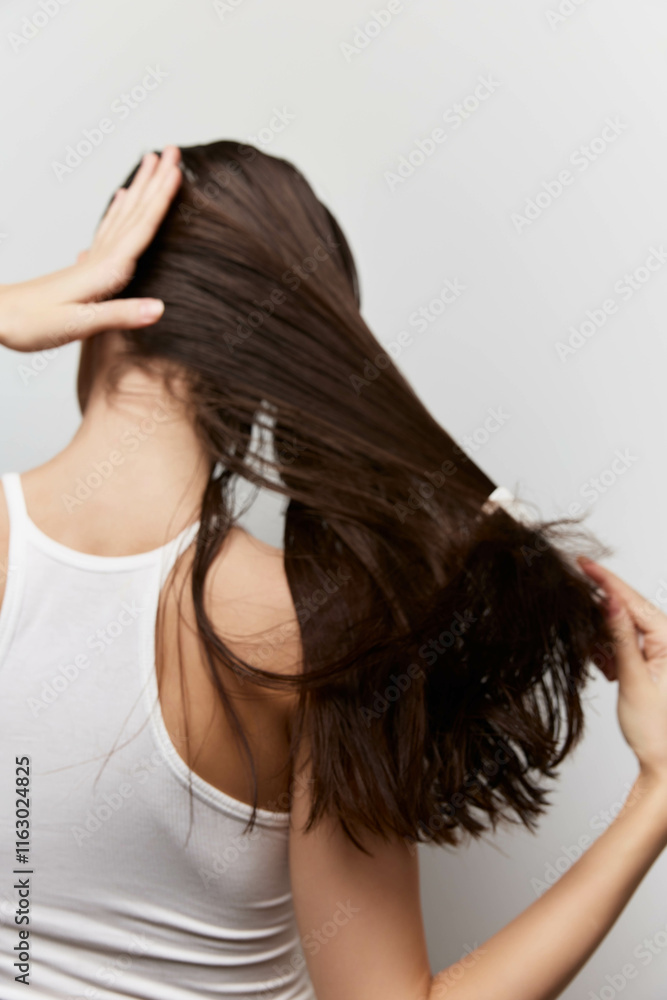 Fototapeta premium Woman with long hair, back view, playing with her hair against a neutral background, showcasing healthy hair texture and movement Ideal for beauty and hair care concepts