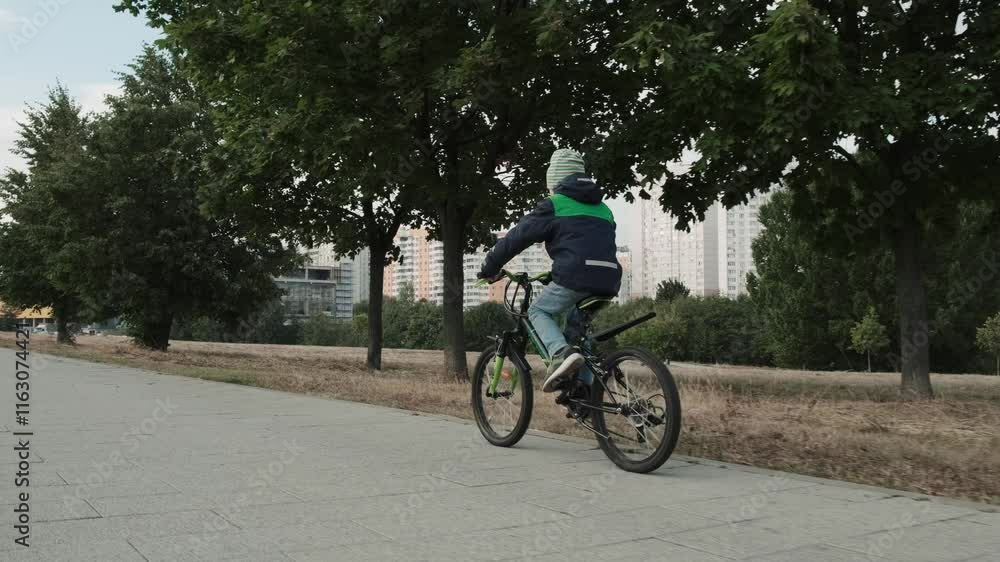 Active teenage little boy riding bike on road in park during cloudy autumn day. Male kid child cycling at street in city, enjoy freedom and happy childhood. Concept travel holidays children lifestyle
