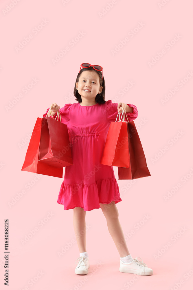 Cute little Asian girl with shopping bags on pink background Cute little Asian girl with shopping bags on pink background
