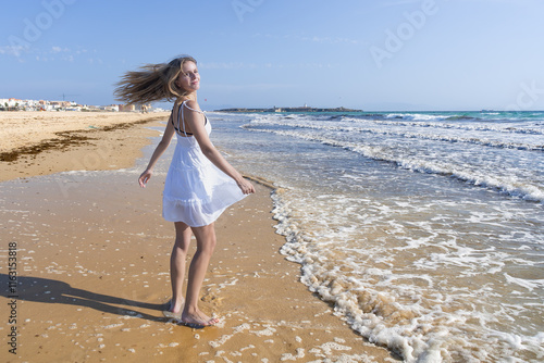 Mujer joven caminando por la playa junto al mar muy alegre y divertida, por su sensacional día de vacaciones de verano en la playa, un día soleado con cielo azul. photo