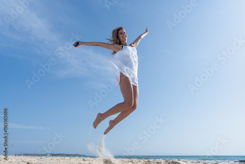 Mujer joven saltando de emoción porque esta feliz y divertida, con un sensacional día de vacaciones en verano en la playa, soleado con cielo azul. photo