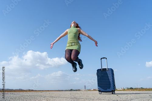 Viajera saltando de alegría como si volara en el aire con los brazos abiertos porque se va de viaje en avión un día soleado de verano con cielo azul y nubes.