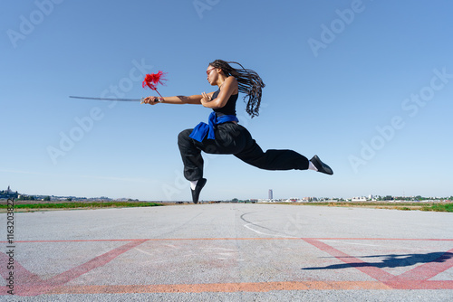 Chica experta en artes marciales haciendo un ataque saltando en el aire, en el paisaje infinito y minimalista de una pista de aterrizaje, un día soleado de verano con cielo azul. photo