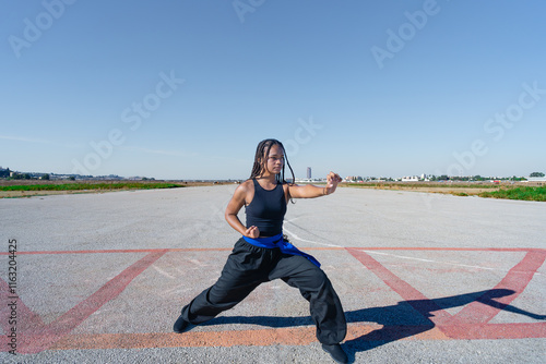 Chica joven luchadora de artes marciales en el paisaje infinito y minimalista de una pista de aterrizaje un día soleado de verano con cielo azul. photo