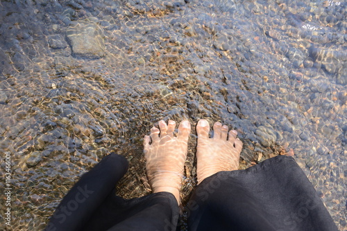 top view of feet soaking in fresh flowing water, Feet in cold clear and clean water feel relaxed and fresh, Relaxing by the sea. Barefoot woman's feet standing in water.