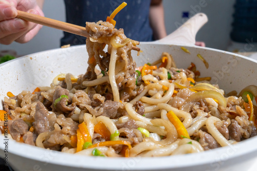  Close-up of beef udon noodles being lifted with chopsticks from a pan photo