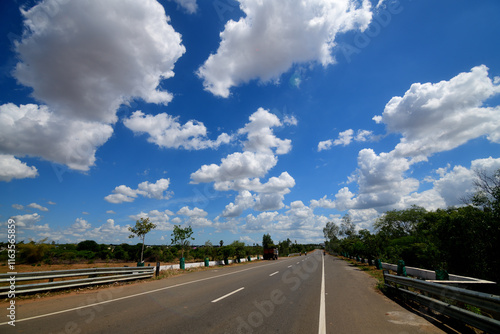 A long road under a blue sky with fluffy clouds