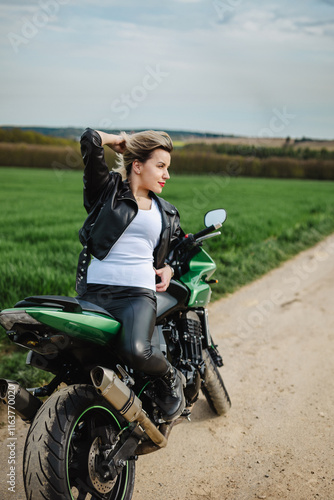 Confident woman seated on a green motorcycle, dressed in a black leather jacket and matching pants. Perfect for themes of adventure, style, and freedom. photo