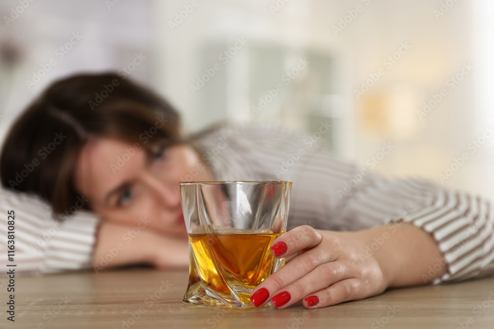 Alcohol addiction. Woman with glass of whiskey at wooden table indoors, selective focus Alcohol addiction. Woman with glass of whiskey at wooden table indoors, selective focus