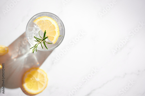 Top view of fresh summer drink - water, lemonade with lemon, rosemary and ice in a glass. Top view, bright background, copy space, summer sun with hard shadows.