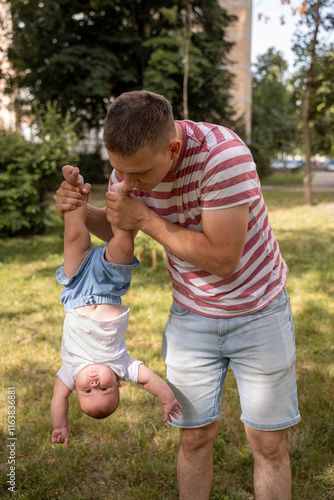 Father holding baby upside down. Father and daughter relationship. Unusual form of education. Non-traditional growing up and childhood. Baby swallow foreign object.  