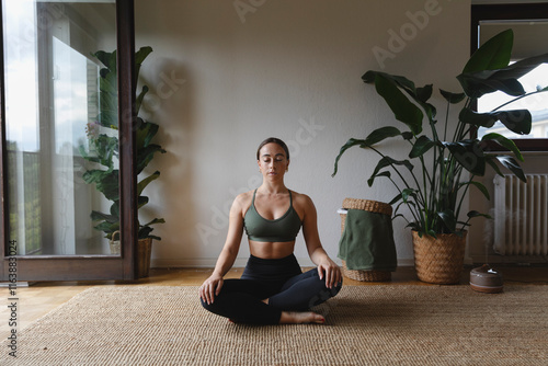 Woman sitting cross-legged and meditating on rug at home
