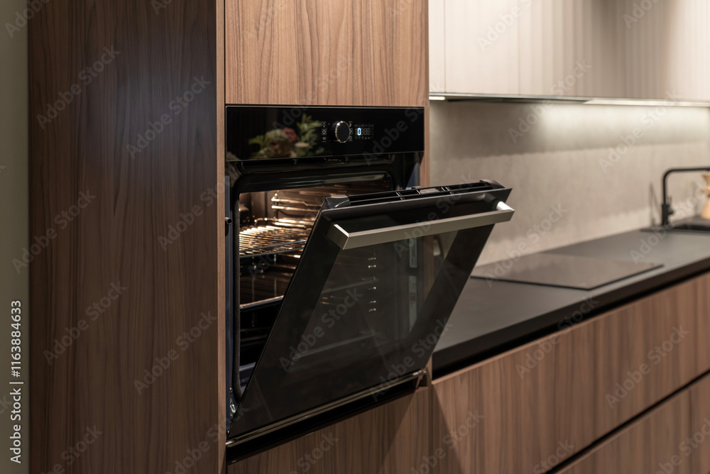 Fototapeta premium Modern opened built-in oven in dark wooden kitchen cabinet