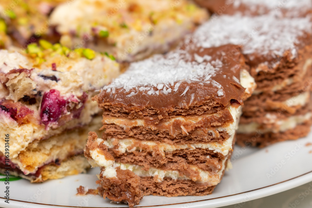 Plate of desserts with a piece of chocolate cake on top. The cake is covered in chocolate and has a white frosting. There are also other desserts on the plate, including a piece of cake with nuts Plate of desserts with a piece of chocolate cake on top. The cake is covered in chocolate and has a white frosting. There are also other desserts on the plate, including a piece of cake with nuts