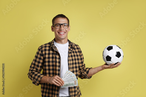 Happy man with money and soccer ball on yellow background