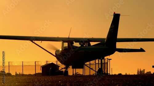 Silhouette of a lightweight turboprop airplane with spinning propeller at sunset or dawn. Scenic cinematic shot of aircraft with the engine running starts moving for take off